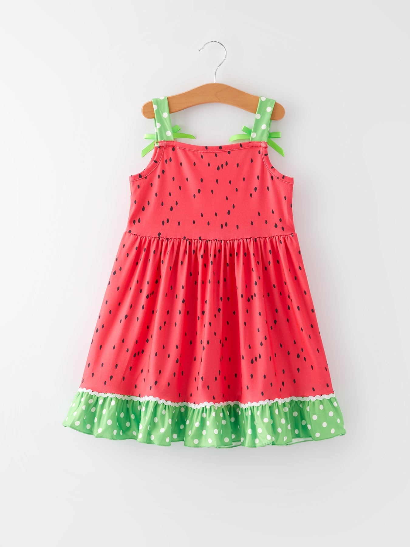 Smiling young girl wearing a pink and green watermelon print suspender dress by Rylee Faith Designs, playing outdoors.