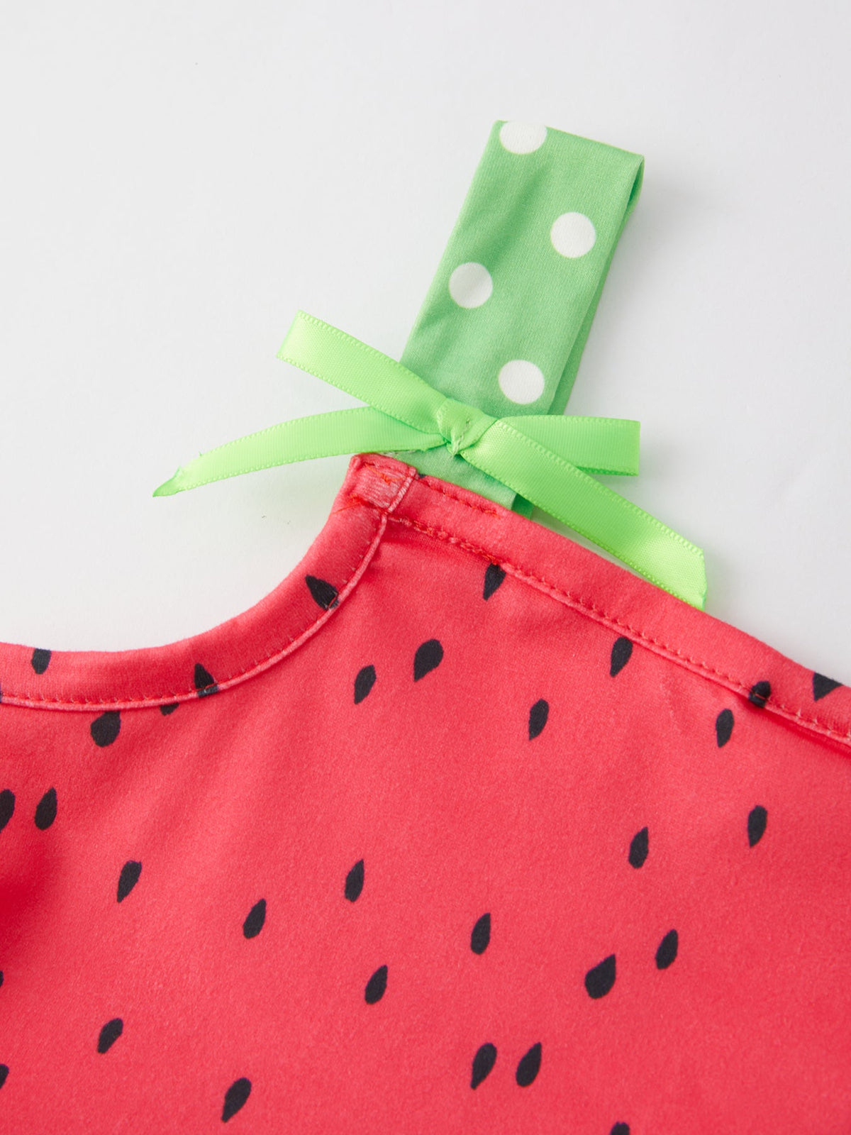 Smiling young girl wearing a pink and green watermelon print suspender dress by Rylee Faith Designs, playing outdoors.