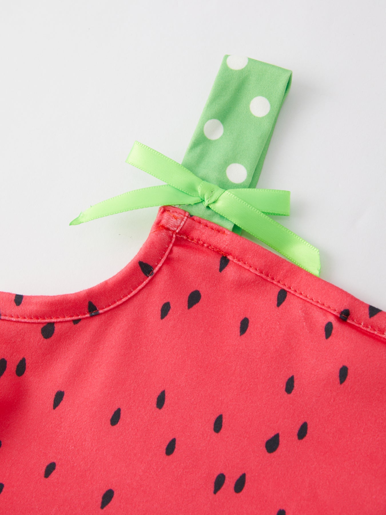 Smiling young girl wearing a pink and green watermelon print suspender dress by Rylee Faith Designs, playing outdoors.