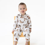 Long sleeve baby romper in a wild horses print, with galloping horses scattered across the fabric and snap closures