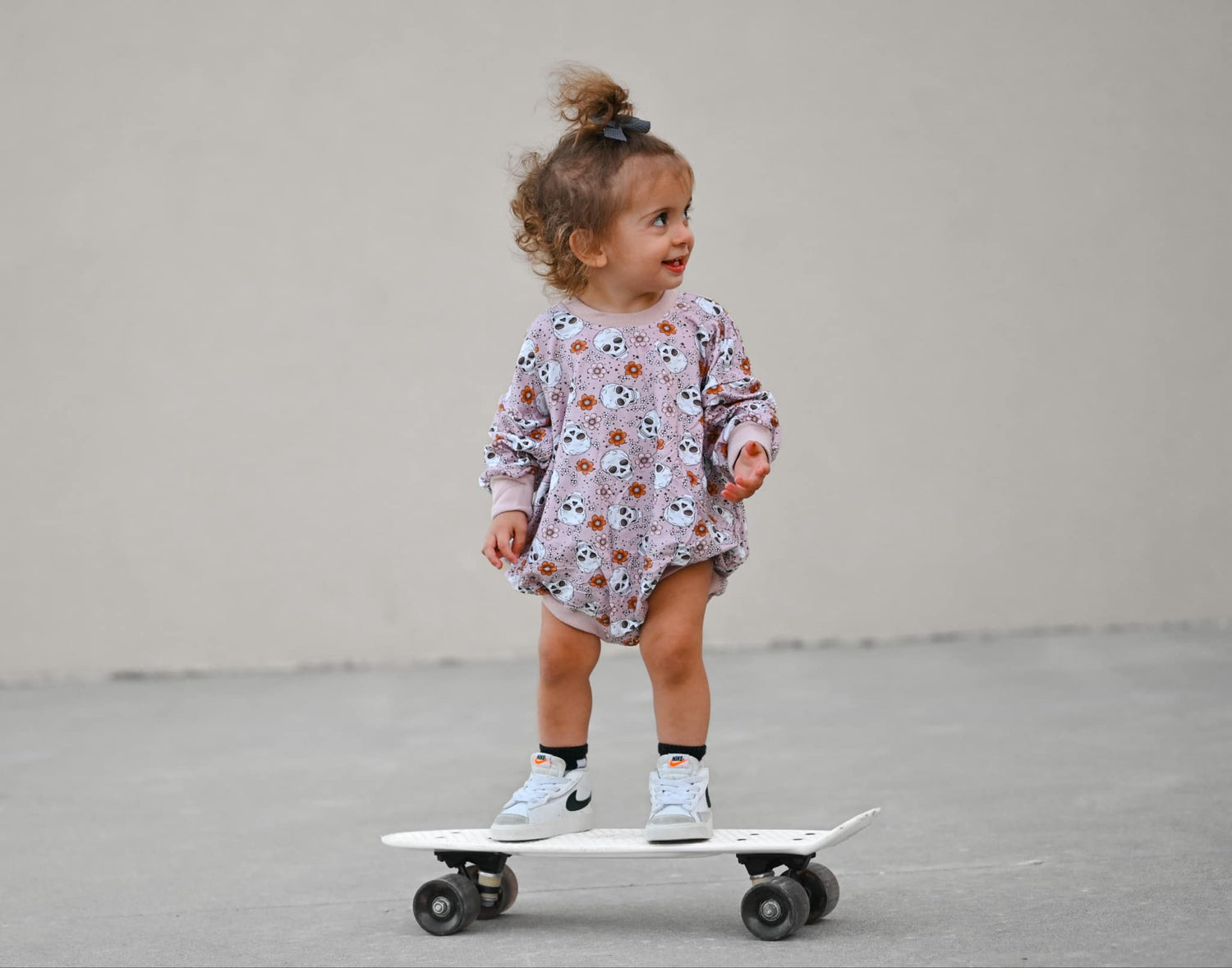 Bubble romper in purple floral skull print with snap closures, shown flat.