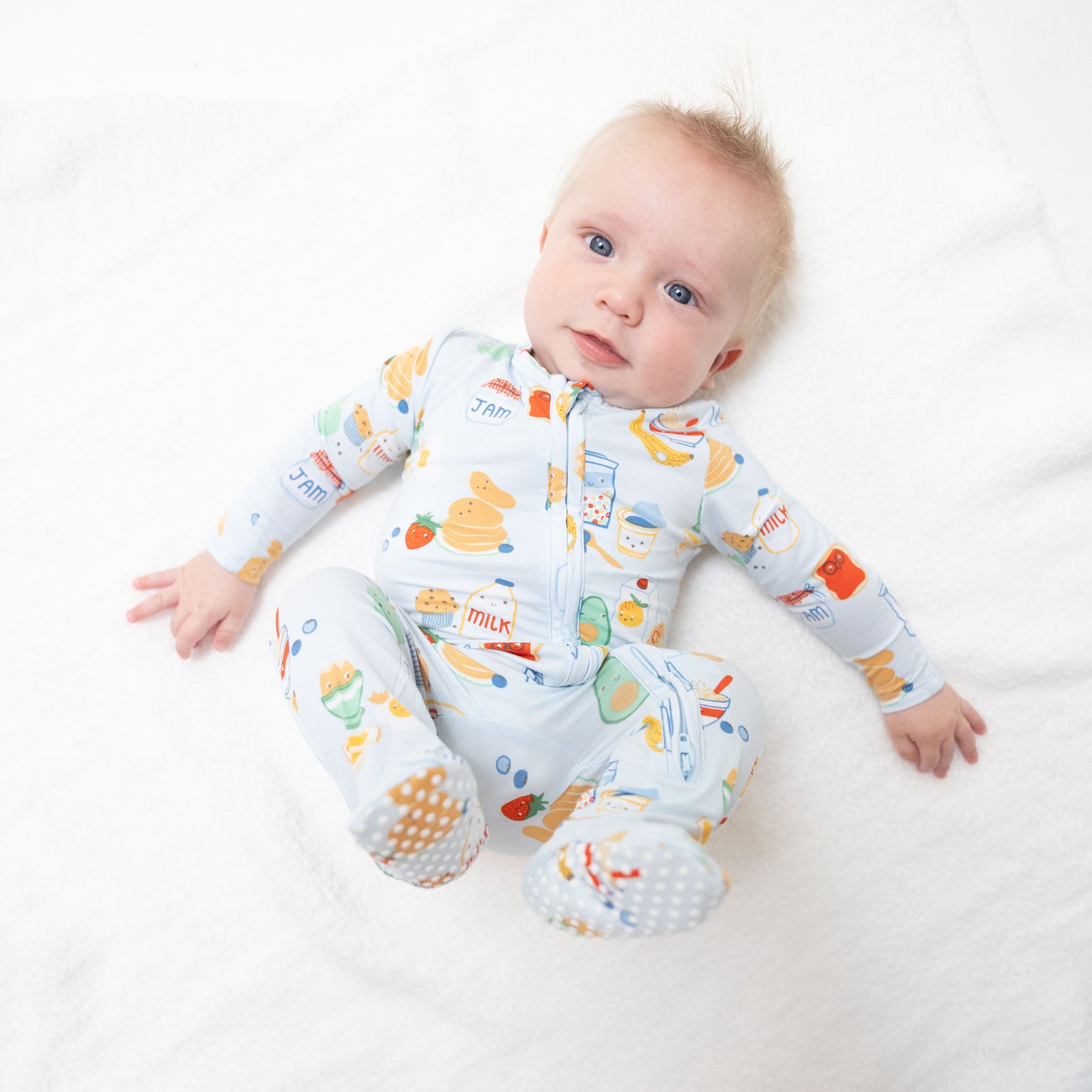 Baby footie pajamas in blue with a breakfast-themed print, featuring a full two-way zipper and footed legs.