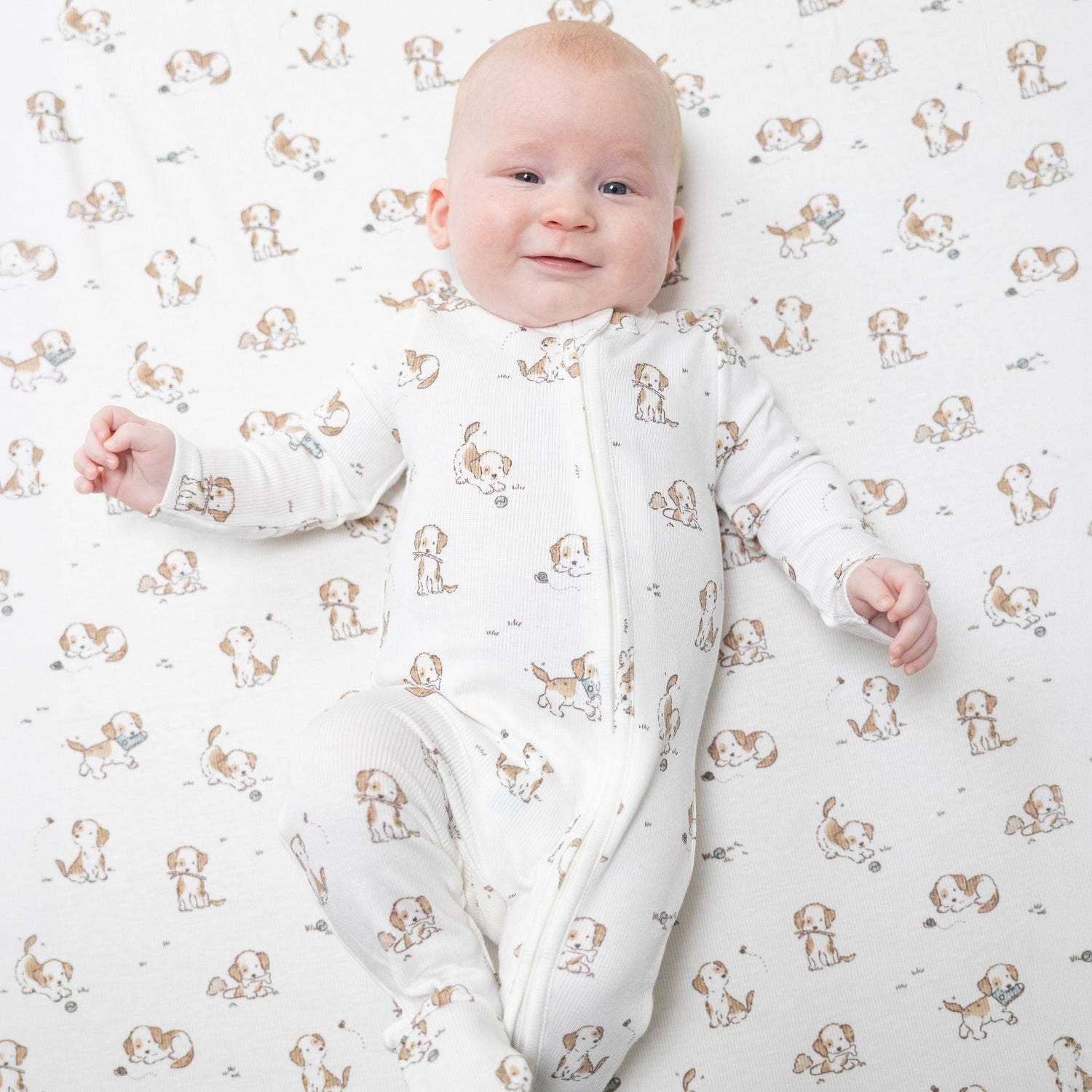 Blue zip-front baby footie with an explorer puppy print, footed legs, and grippers on the soles