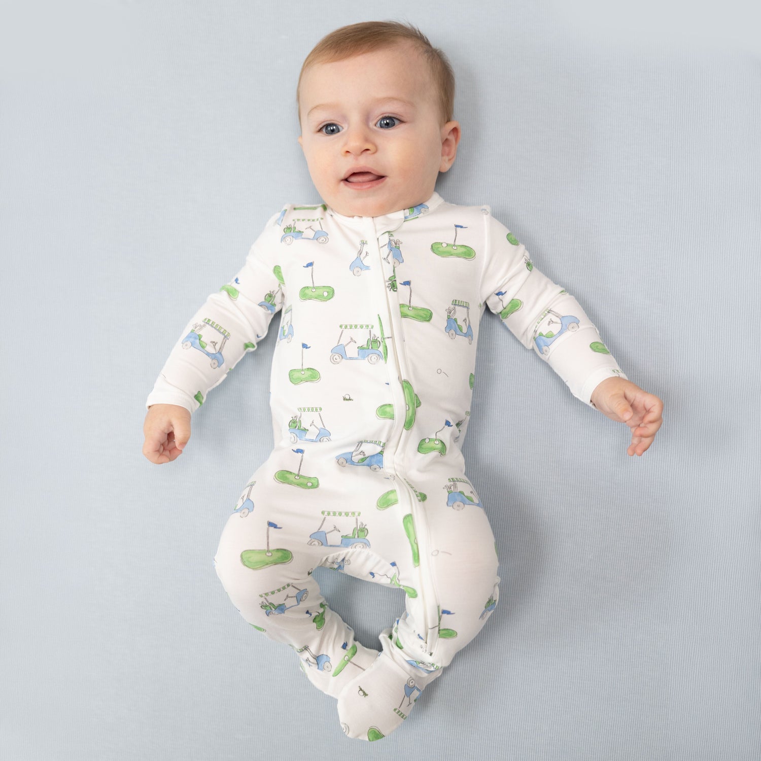 Baby footie pajamas in blue with a golf cart print, two-way zipper, footed legs, and grippers.