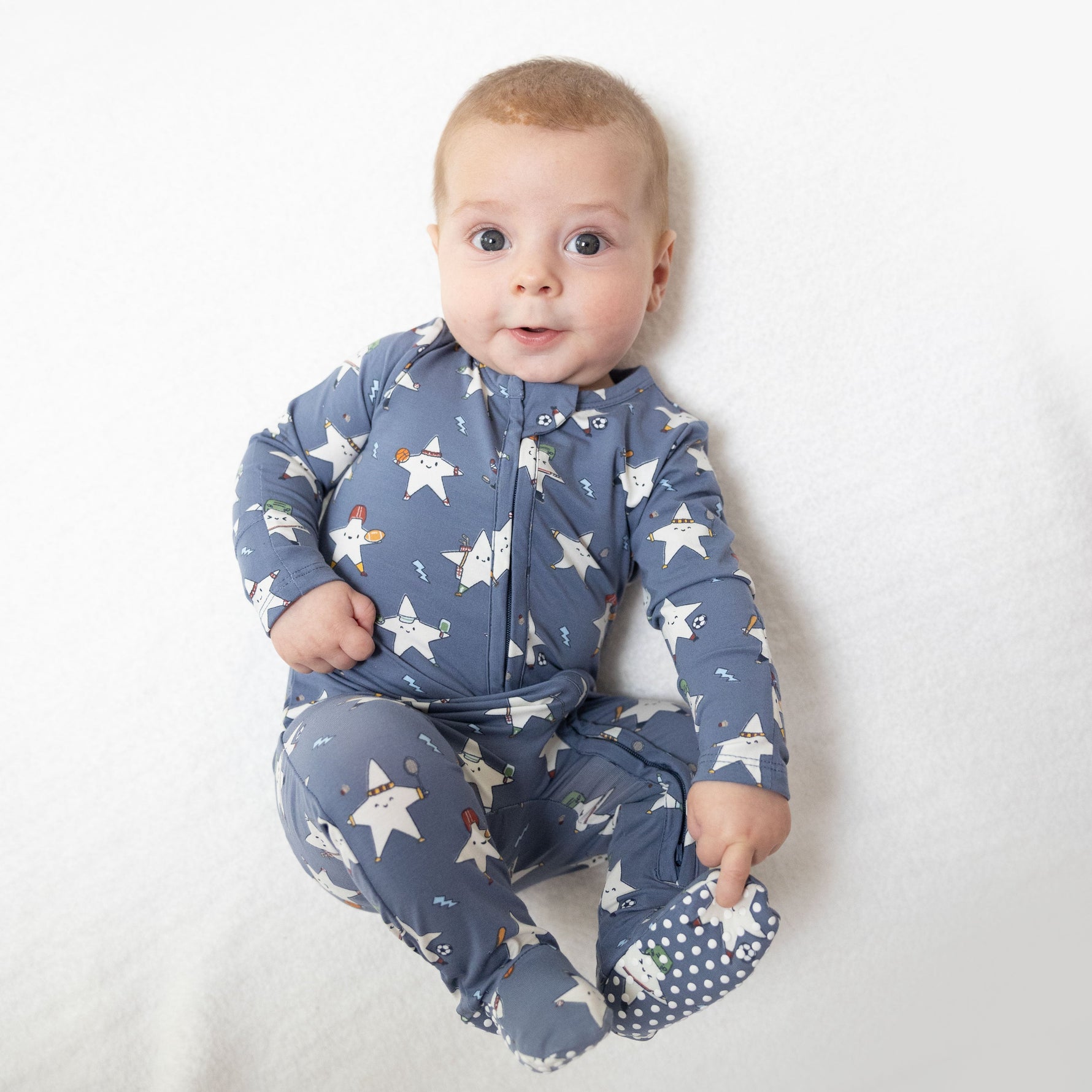 Baby footie pajamas in a sports all-stars print that glows in the dark, with a two-way front zipper and footed legs.