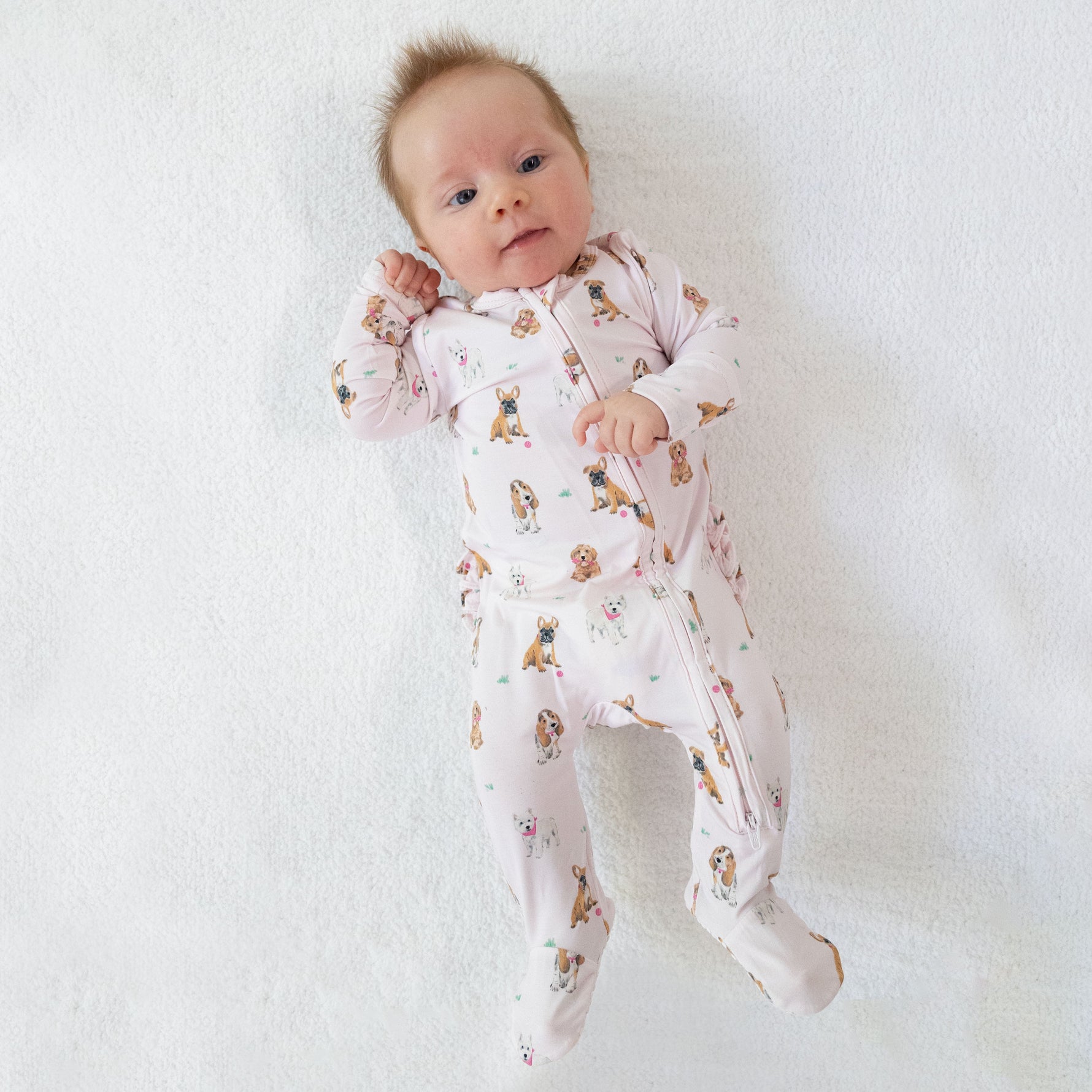 Pink baby footie with playful dog print, a ruffle back detail, and full-length two-way zipper.