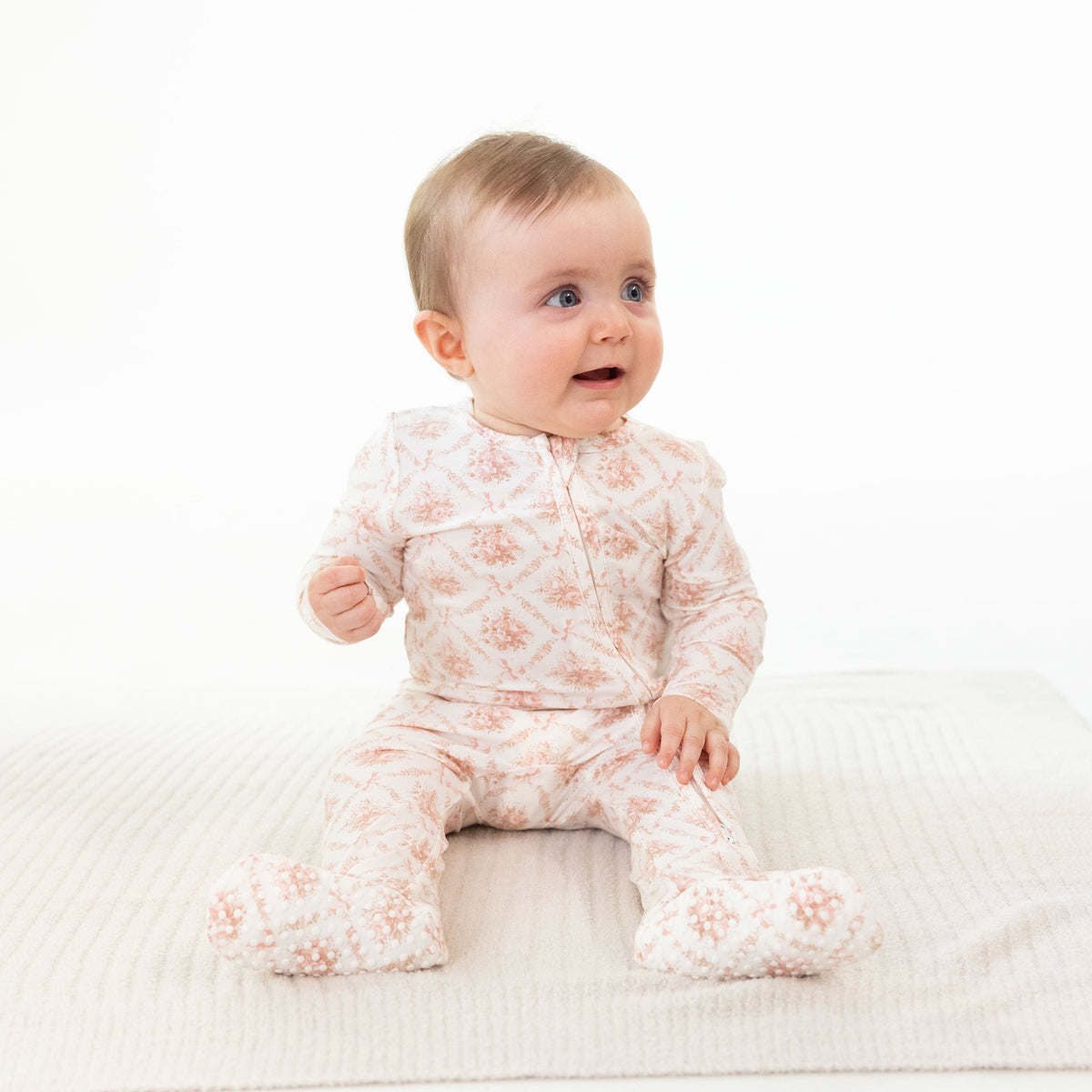 Footie pajamas in a rose bow lattice print with a ruffle back detail and full-length zipper