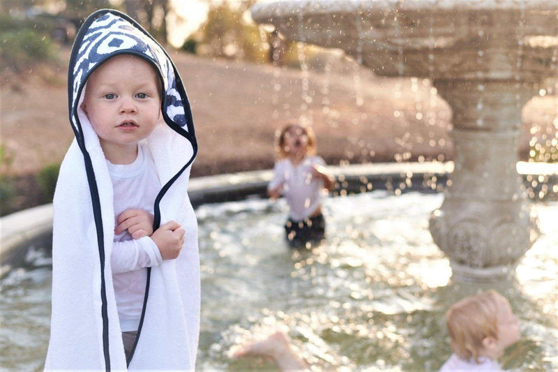 Child wrapped in a Moroccan Blue cotton hooded towel near a fountain.