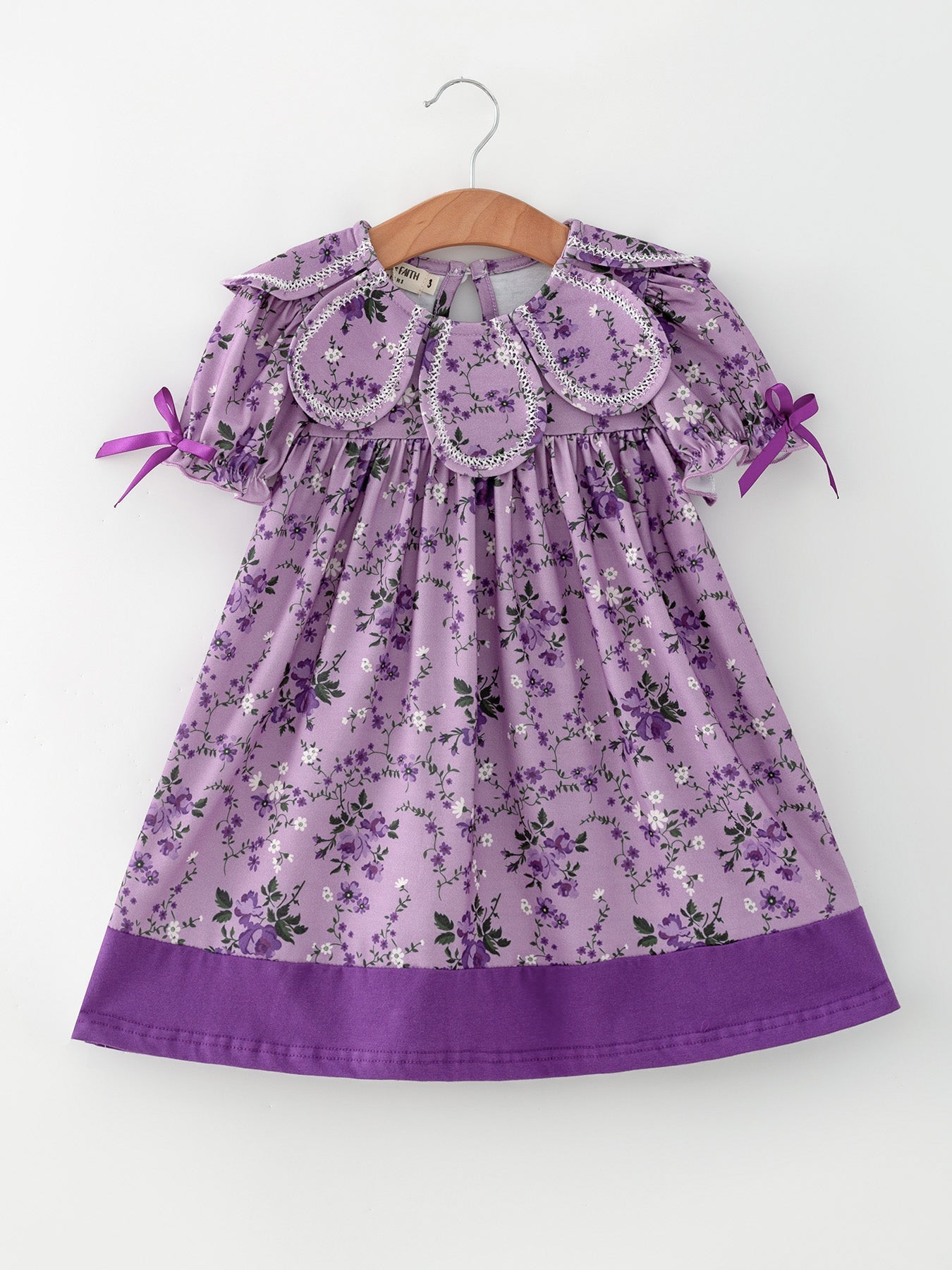 Purple floral girls' dress with petal collar, contrast piping, side sleeve bows, and a gathered ruffle hem