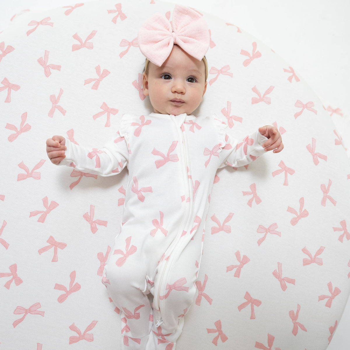 Baby footie pajamas in a Pretty Bows print with ruffle sleeves, front zipper, and footed grippers.