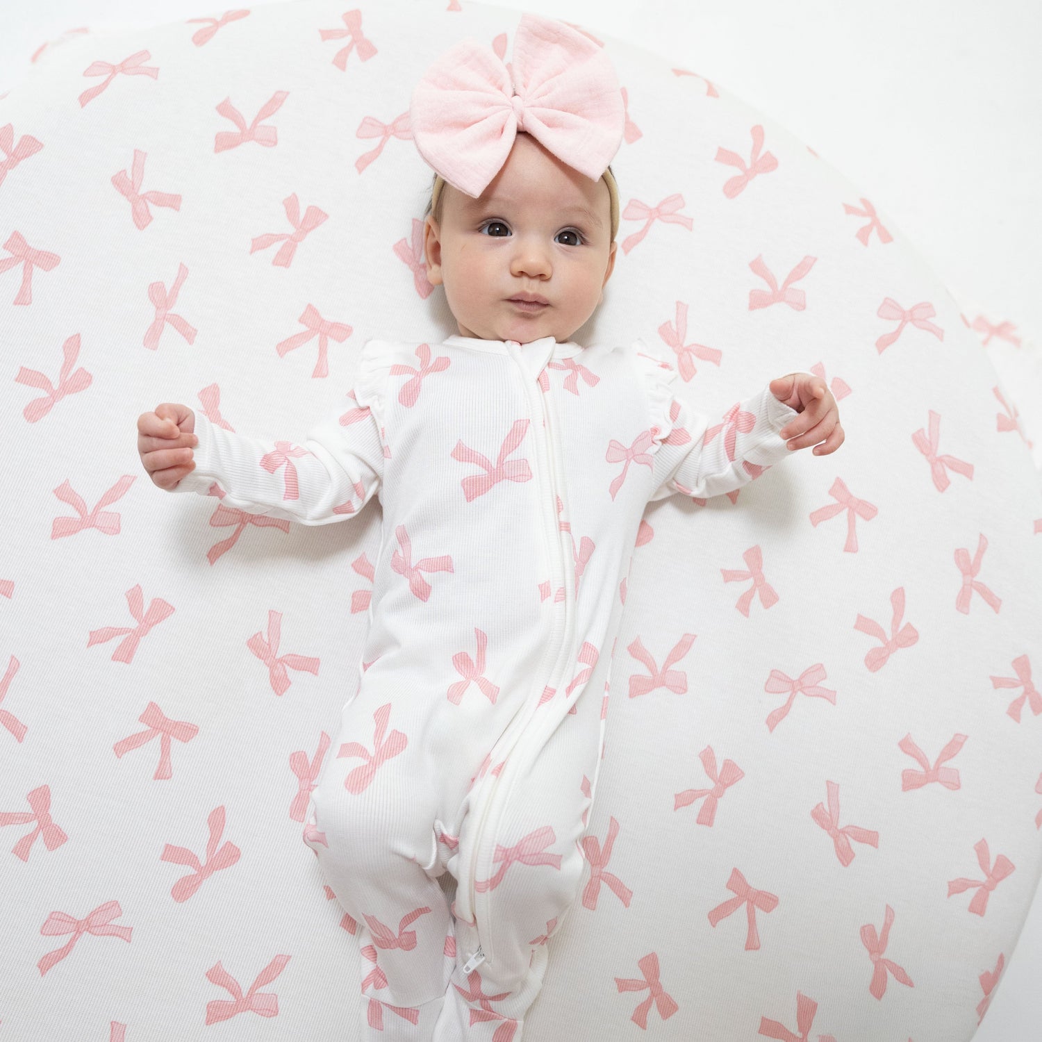 Baby footie pajamas in a Pretty Bows print with ruffle sleeves, front zipper, and footed grippers.