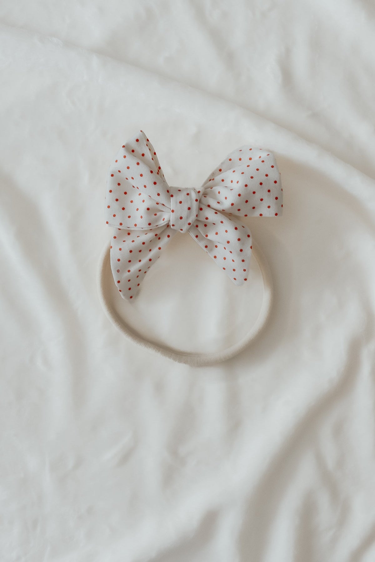 Close-up of a baby wearing a soft ruby red knit headband by Little Mae & Co, on a light background.