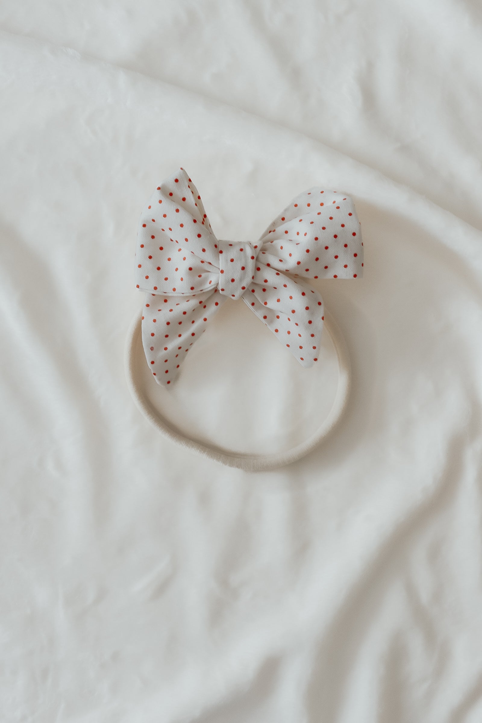 Close-up of a baby wearing a soft ruby red knit headband by Little Mae & Co, on a light background.