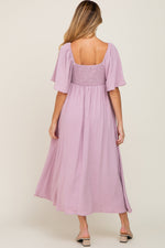 Pink textured dot maternity midi dress with front tie and ruffle sleeves.