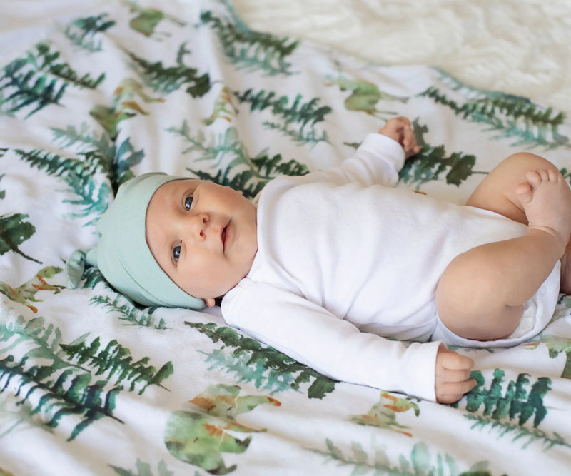 Baby lying on a forest-themed minky blanket, ideal for newborns to toddlers.
