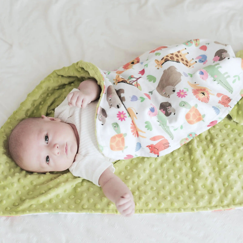 Baby lying on a zoo animal print minky blanket, ideal for toddlers and newborns.
