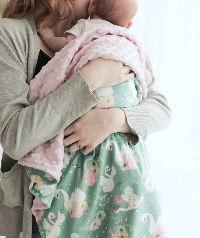 Baby being held in floral swan-patterned minky blanket.