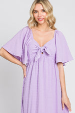 Baby girl wearing a lavender textured dot midi dress with front tie and ruffle sleeves.