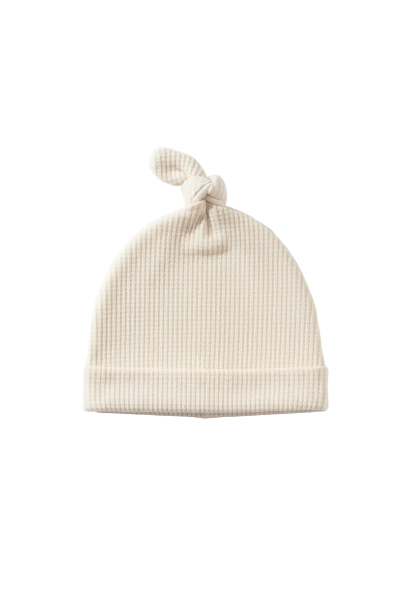 Soft cream waffle knit knot hat for newborns, featuring a tied top and gentle texture.