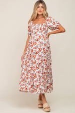 Full-length view of a pregnant woman in a cream floral smocked square neck tiered maternity maxi dress.