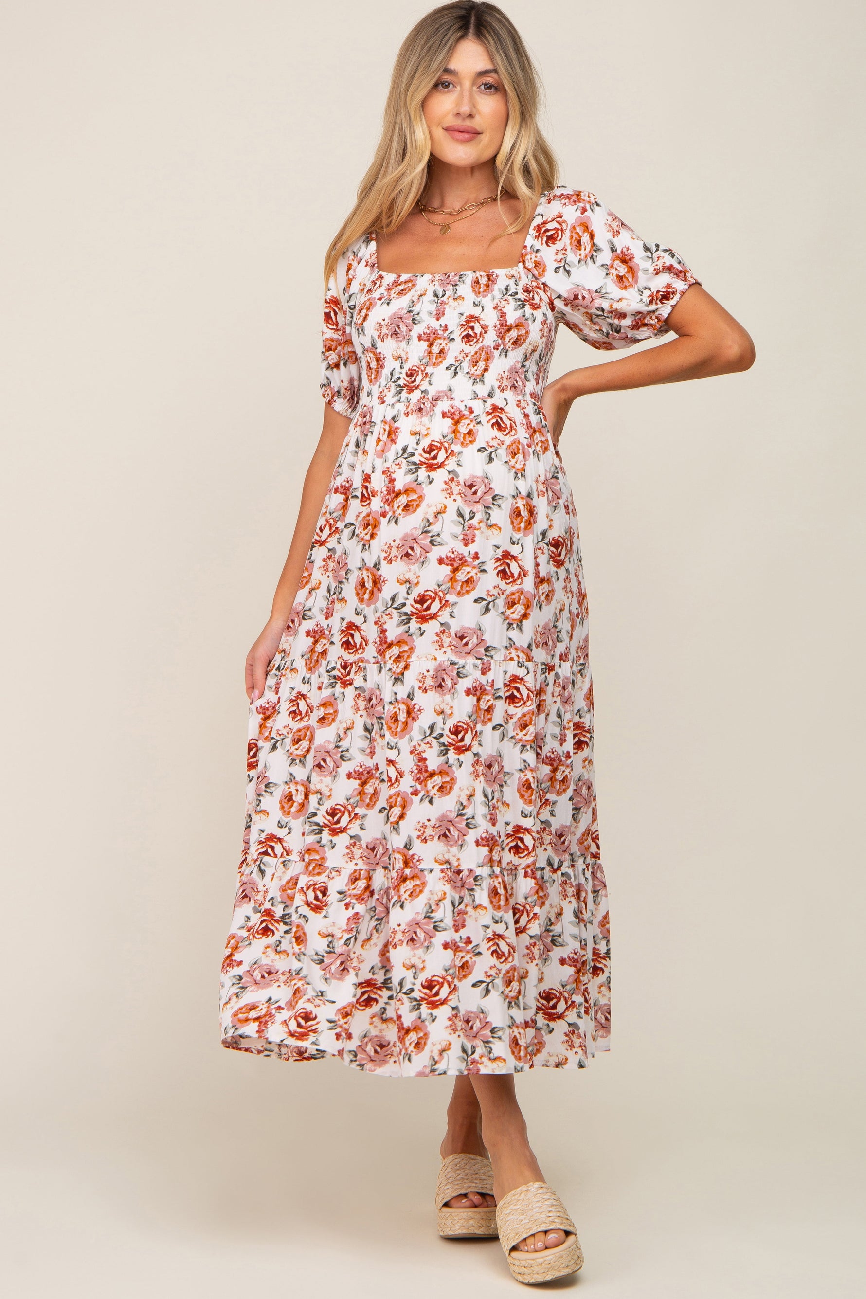 Full-length view of a pregnant woman in a cream floral smocked square neck tiered maternity maxi dress.