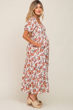 Full-length view of a pregnant woman in a cream floral smocked square neck tiered maternity maxi dress.