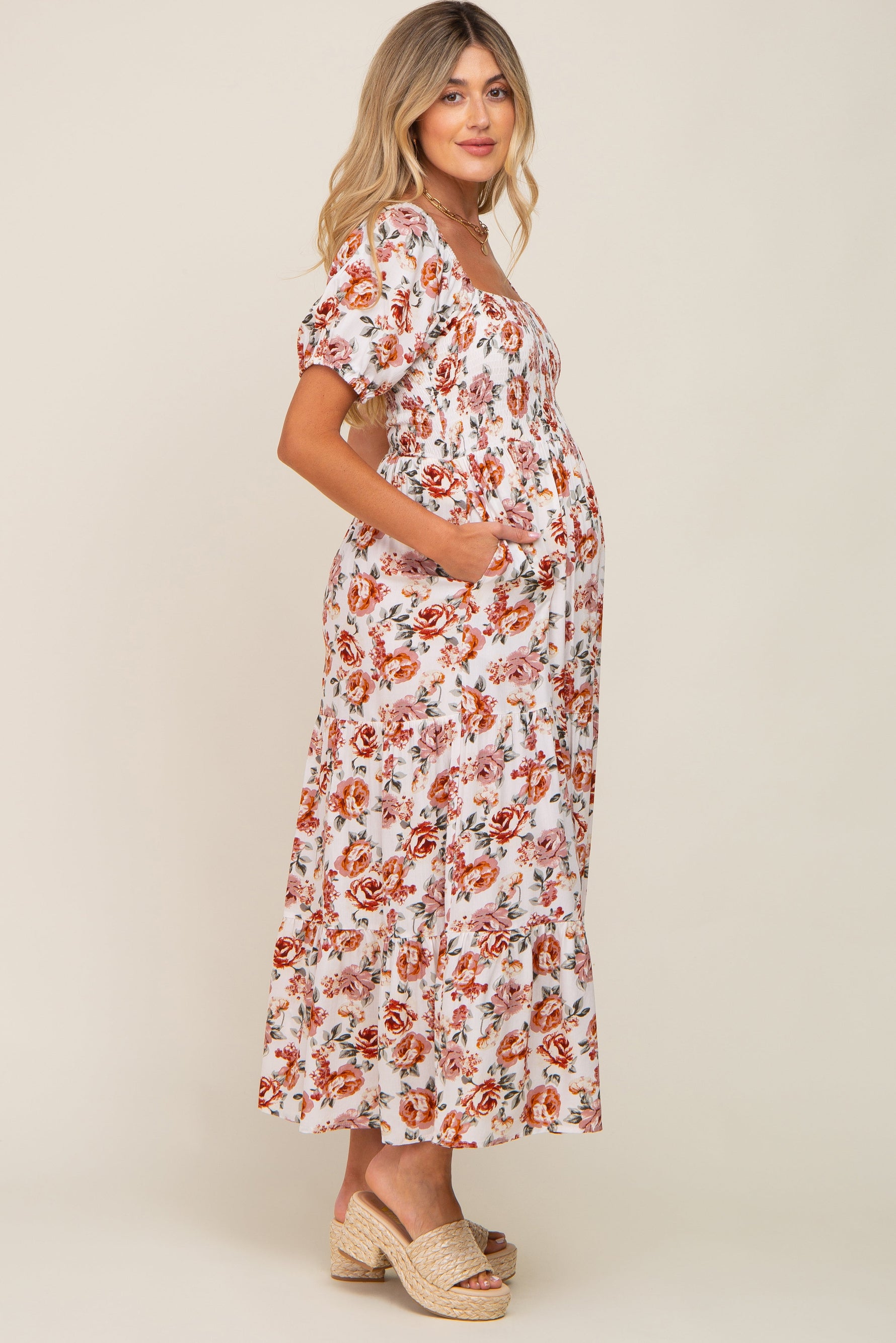 Full-length view of a pregnant woman in a cream floral smocked square neck tiered maternity maxi dress.