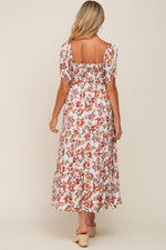 Full-length view of a pregnant woman in a cream floral smocked square neck tiered maternity maxi dress.