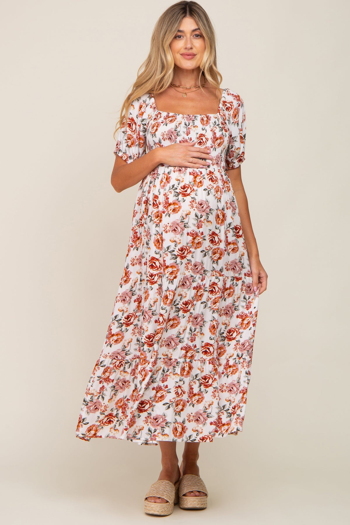 Full-length view of a pregnant woman in a cream floral smocked square neck tiered maternity maxi dress.