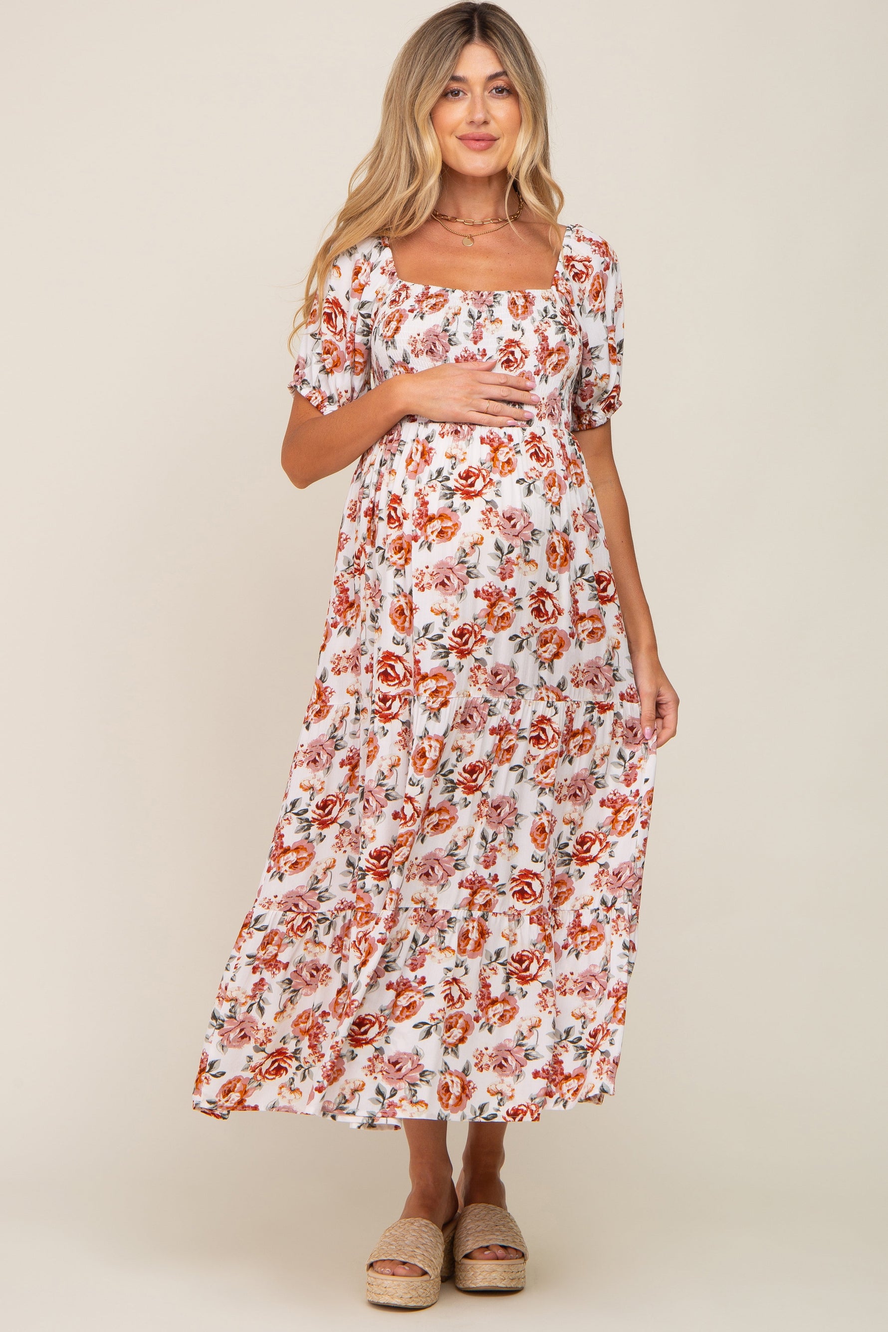 Full-length view of a pregnant woman in a cream floral smocked square neck tiered maternity maxi dress.