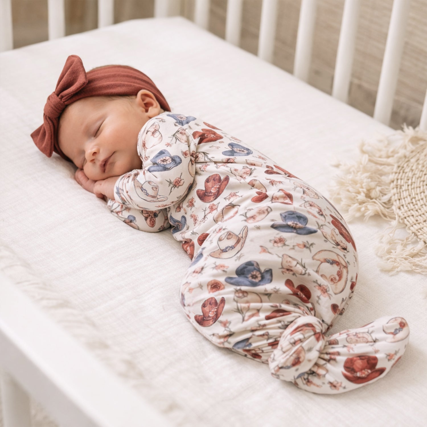 Newborn knotted gown with a sketch-style print of cowgirl hats and flowers in muted desert tones.