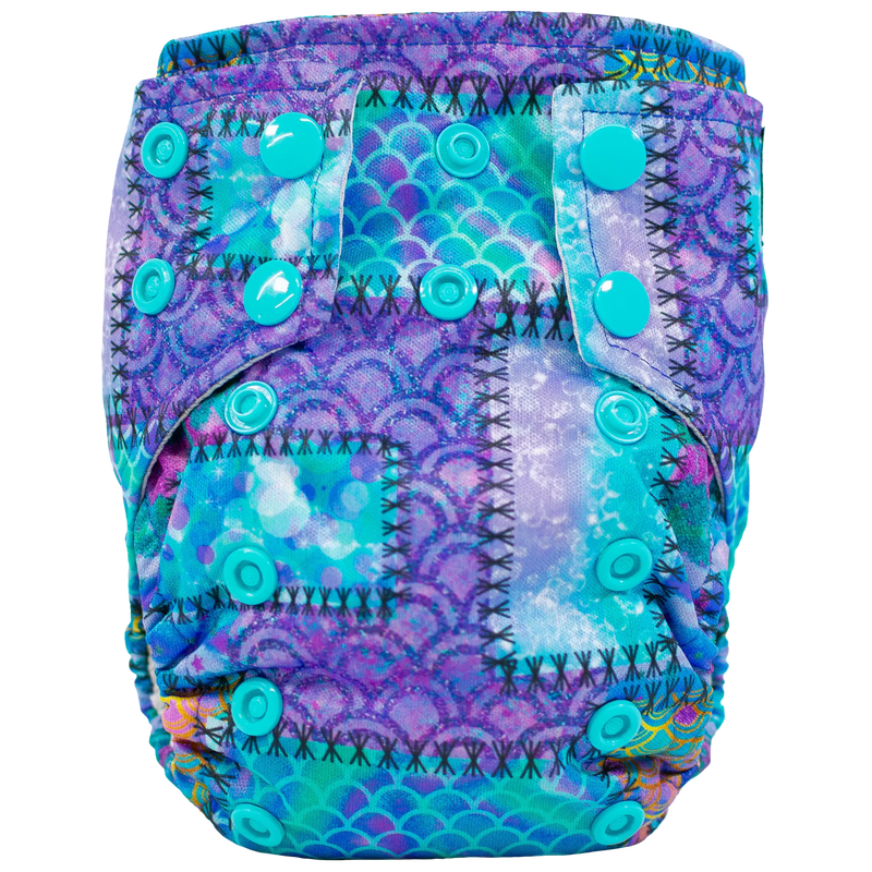 Tiny Tushies Newborn AIO Cloth Diaper with colorful snaps and printed design, suitable for 5-20 lbs, with pocket opening for inserts.
