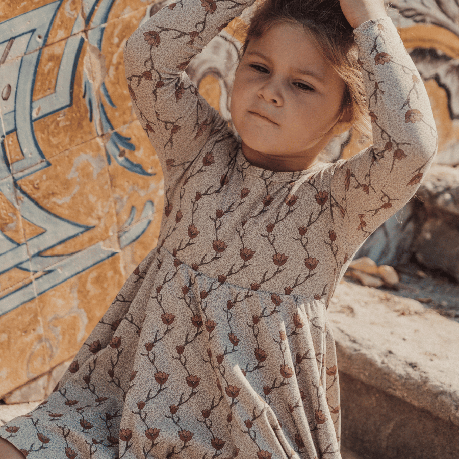 Young girl wearing a vibrant Iris print long sleeve dress, twirling happily in a sunny field.
