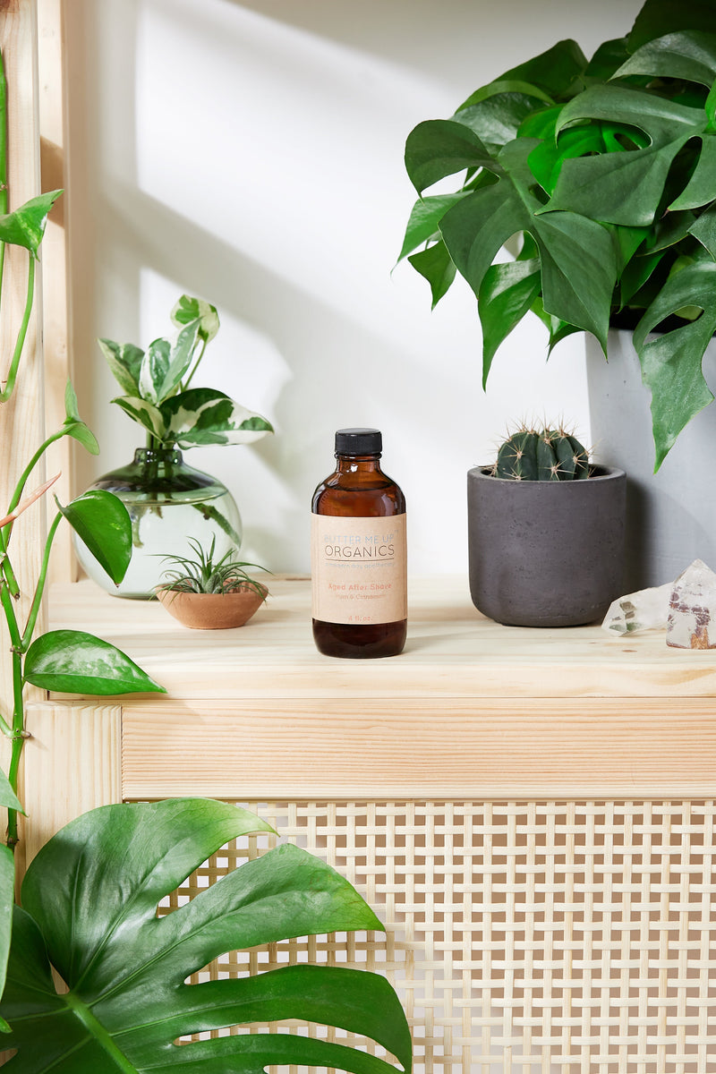 Natural aged aftershave cologne bottle on wooden shelf, surrounded by green plants.