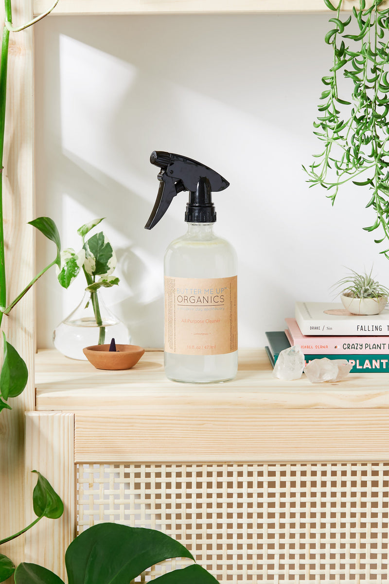 Natural All Purpose Cleaner in glass bottle with spray pump on wooden shelf, surrounded by plants and decor items.