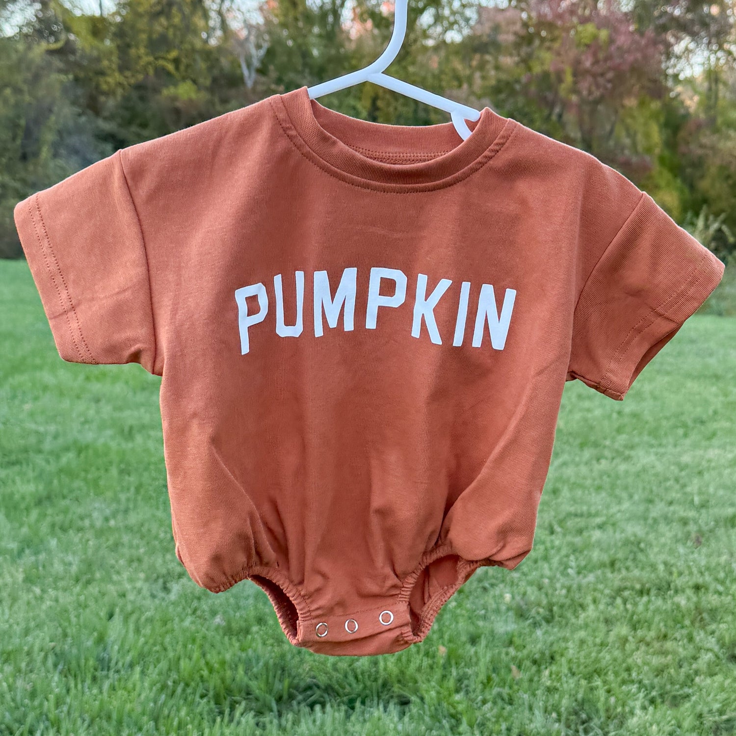Baby bubble romper with screenprinted PUMPKIN graphic, shown in white and orange with rolled sleeves and snaps at the crotch.