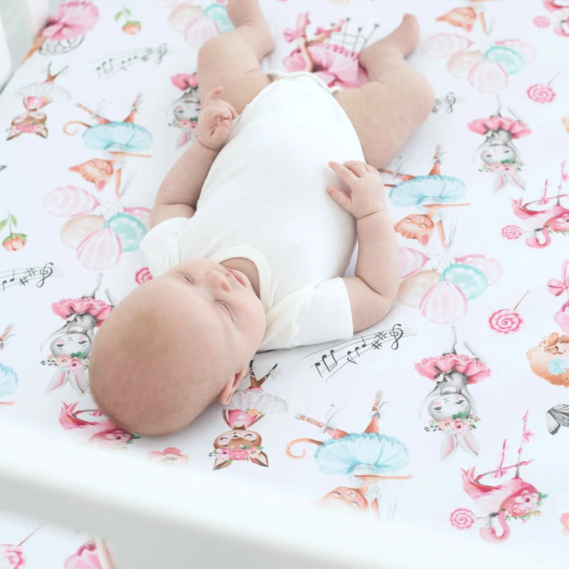 Ballerina patterned fitted crib sheet with a baby lying on it.