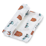 Organic cotton muslin swaddle blanket printed with tractors and barns, spread flat to show the farm design