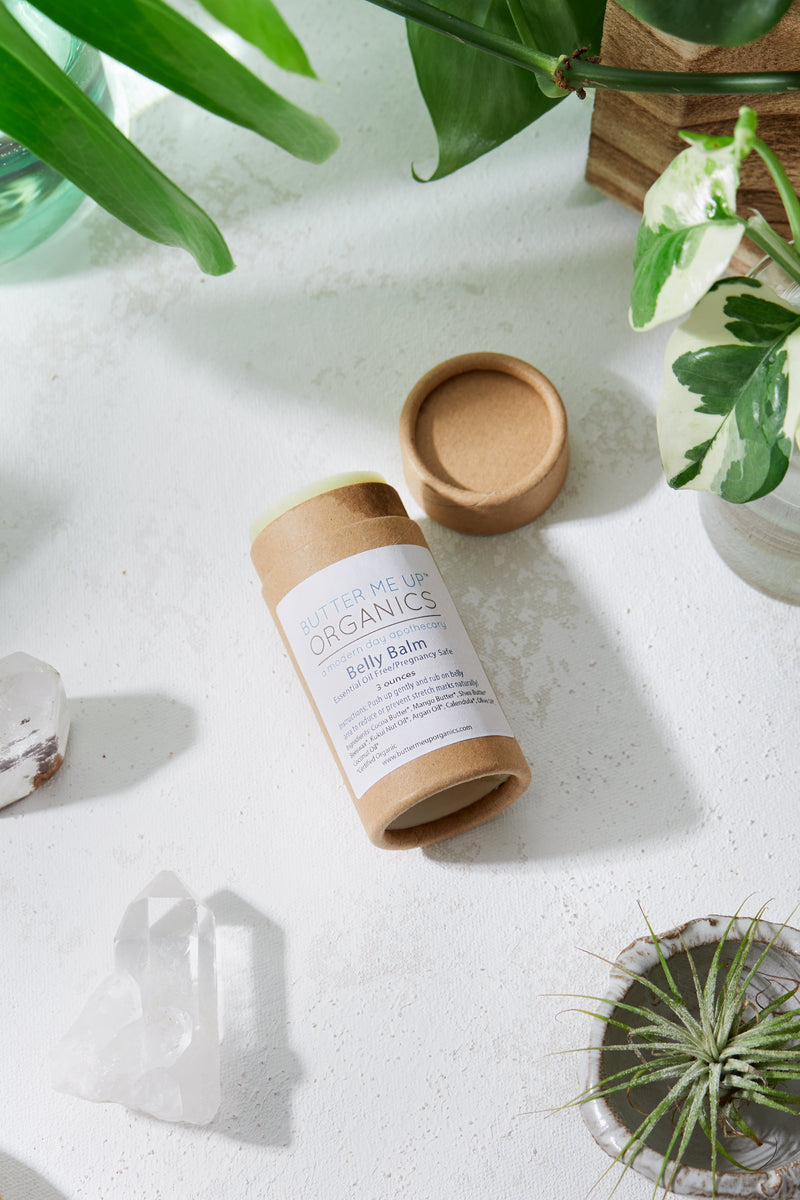 Organic pregnancy balm in eco-friendly packaging on a white surface with plants.