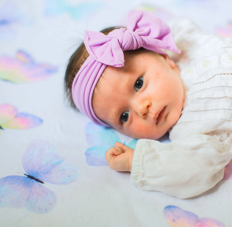 Baby on premium butterfly-themed blanket with purple headband, ideal for nursery.