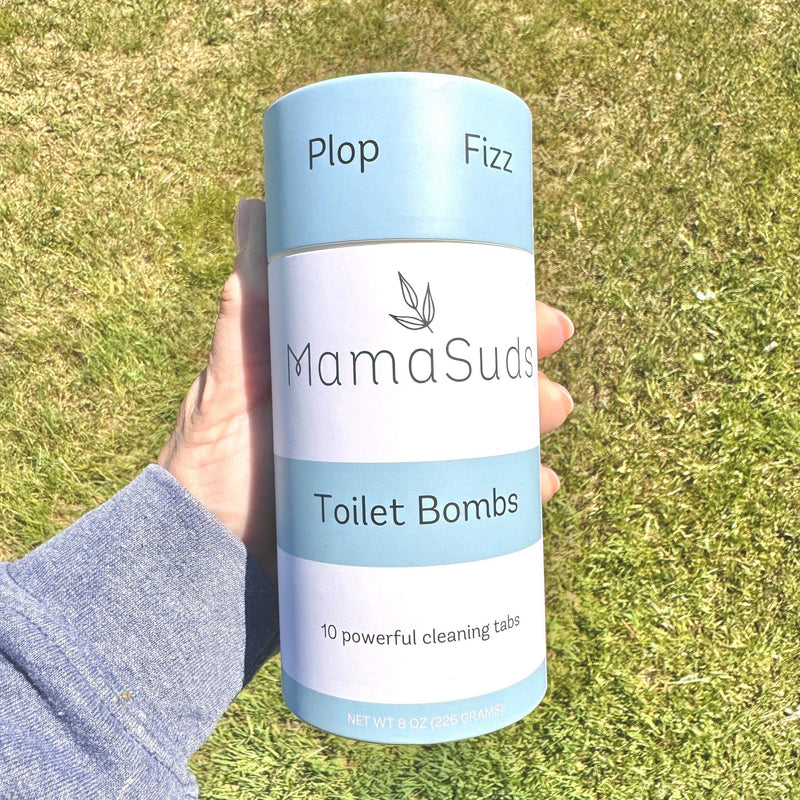 Toilet Bomb Cleaning Tabs in plastic-free packaging held outdoors on grass.