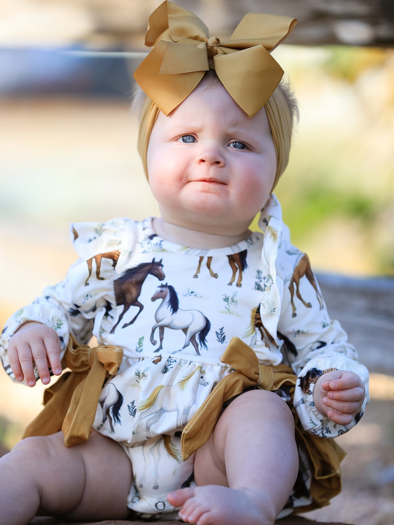 Long-sleeve girls romper with Western horse print, ruffle trim, and a bow accent.