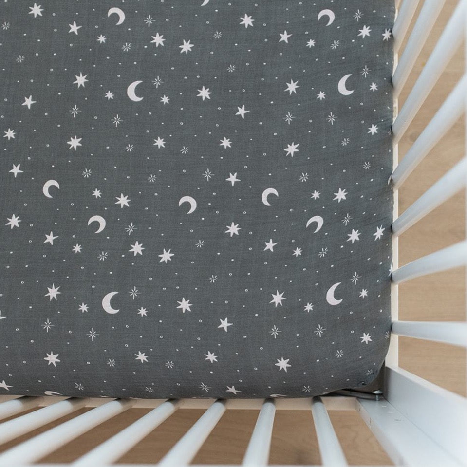 Powder blue muslin crib sheet with a night sky design fitted on a standard crib mattress