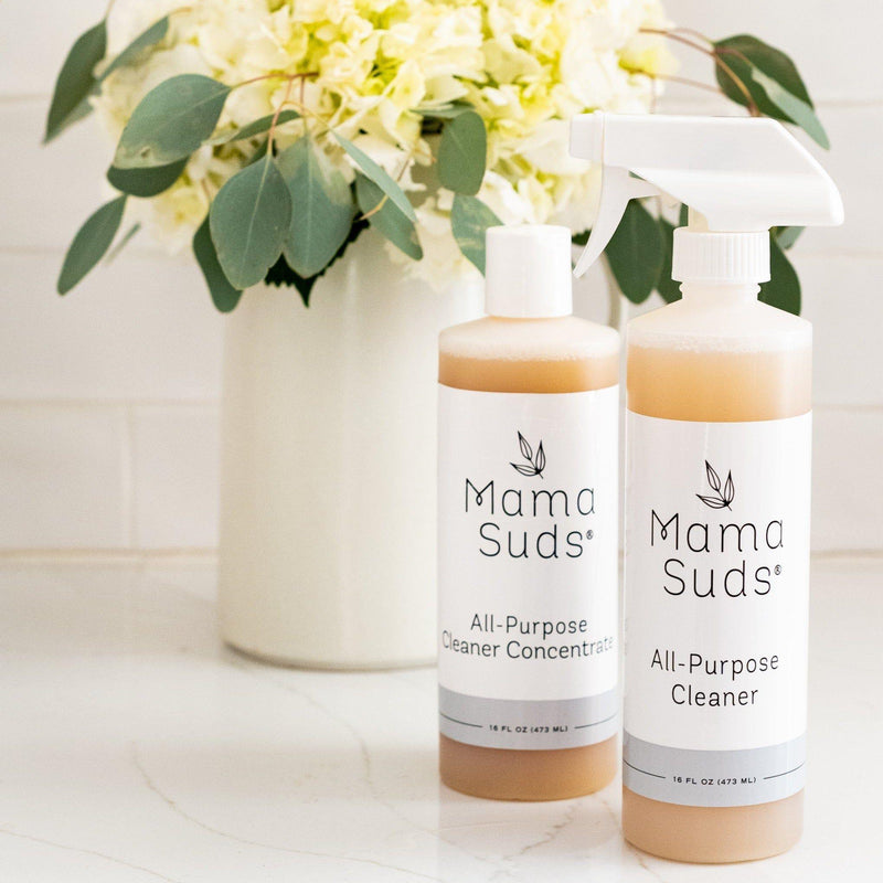 MamaSuds All-Purpose Cleaner and Concentrate bottles displayed on countertop with flowers in background.