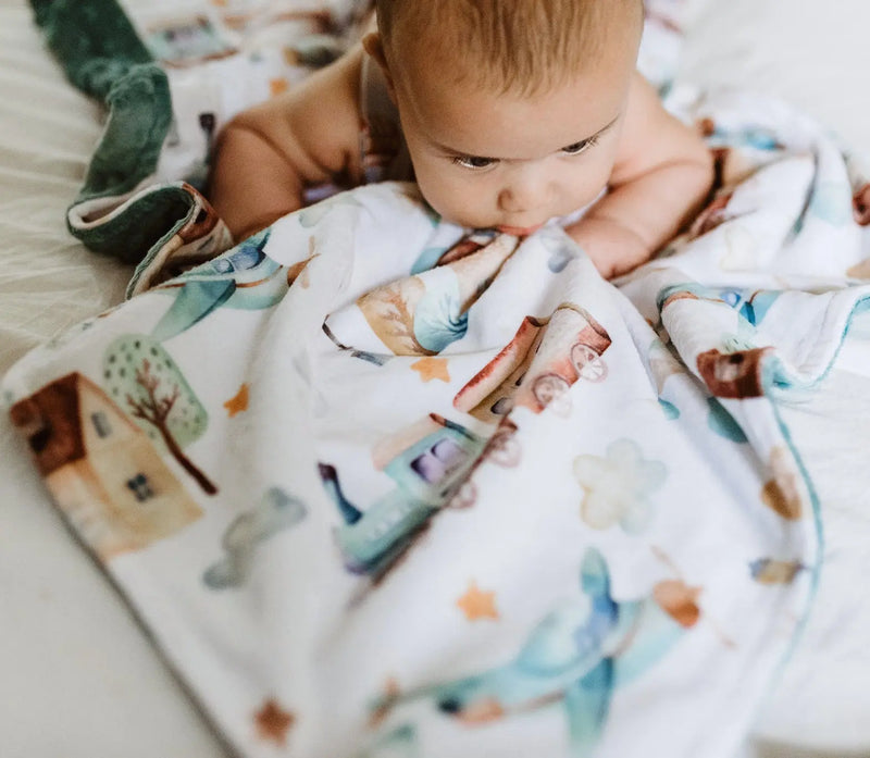 Baby wrapped in premium minky blanket with plane and train pattern.