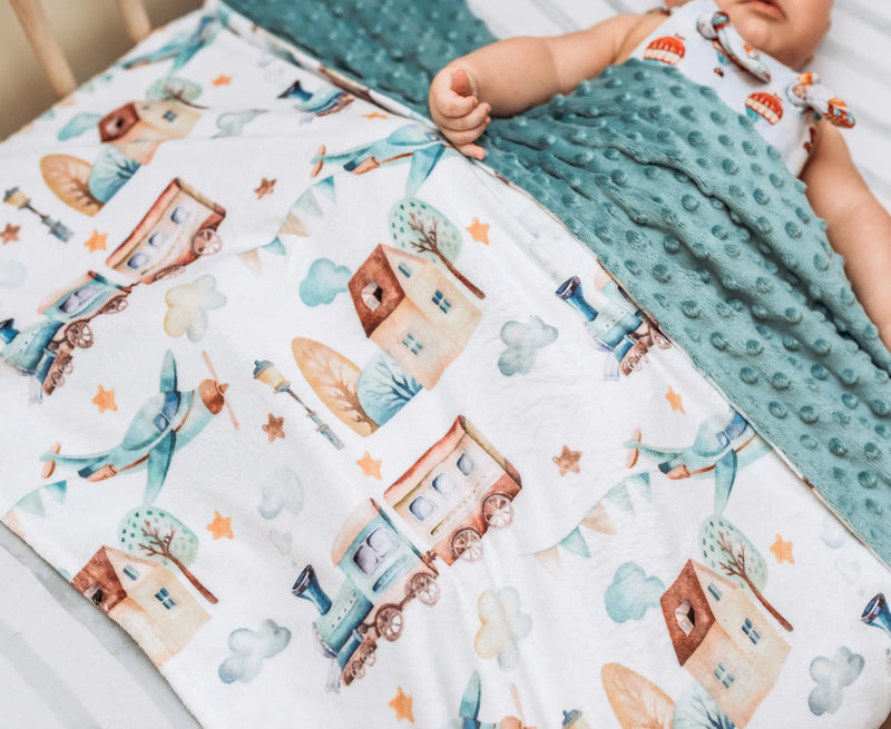 Premium baby & toddler minky blanket with planes, trains, and automobiles pattern on a bed.