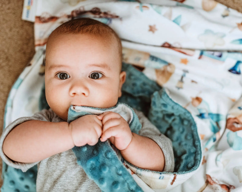 Baby wrapped in a premium minky blanket with planes and trains design.