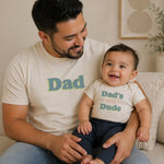 Finn + Emma organic baby bodysuit with 'Dad's Little Dude' graphic print in black on natural cotton.