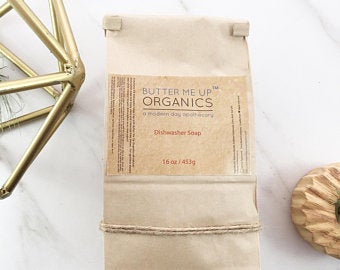All Natural Dishwasher Soap by Butter Me Up Organics in eco-friendly packaging on a marble surface.