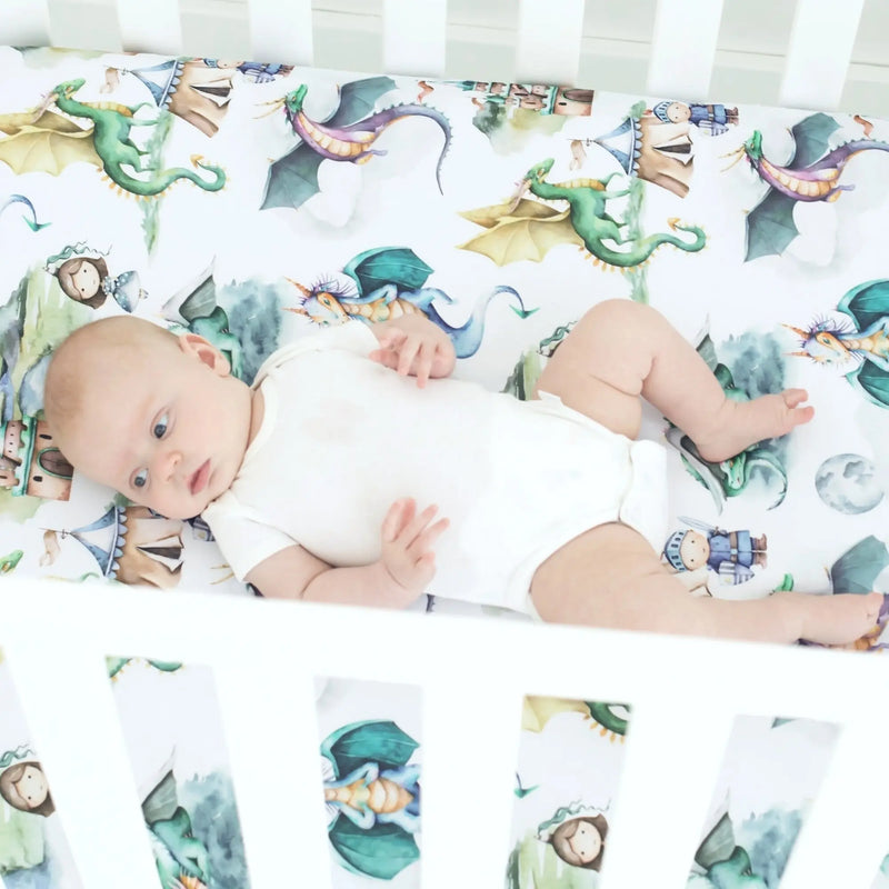 Baby lying on dragons & knights fitted crib sheet in white crib.